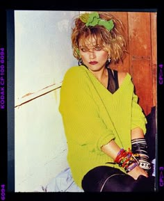 a woman sitting on top of a wooden floor next to a wall and wearing a green sweater