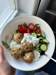 a white bowl filled with meatballs, rice and veggies next to a window