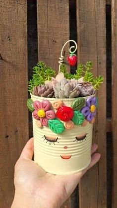 a hand holding a small pot with succulents and flowers on it