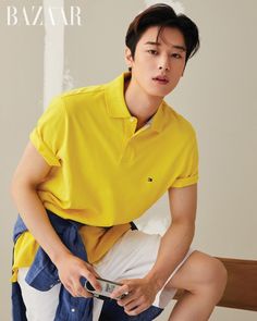 a young man in a yellow shirt and white shorts sitting on a bed holding a cell phone