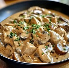 a plate full of mushrooms and gravy with parsley on the top, sitting on a wooden table