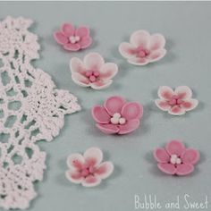 pink and white crocheted flowers are on a gray surface with lace doily