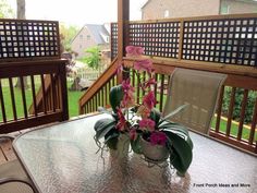 a glass table with flowers on it in front of a wooden deck and fenced yard