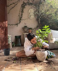 a woman kneeling down next to a potted plant with dirt on the ground in front of her