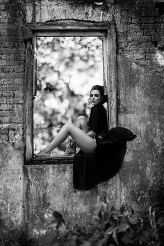 black and white photograph of a woman sitting on a window sill in an old building