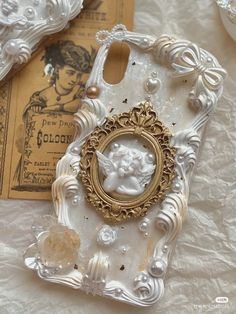 an ornate white and gold cell phone case on a table with other antique items in the background