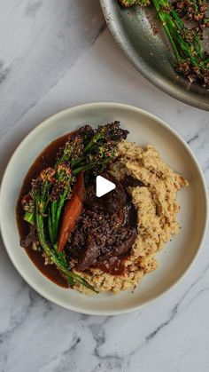 a white plate topped with meat and veggies covered in gravy on top of a marble counter