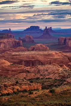 the desert is full of rock formations and green grass in the foreground, under a cloudy sky