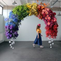 a woman is walking under an arch made out of fake flowers and plastic balls that are hanging from the ceiling