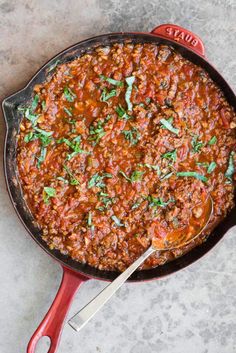 a red skillet filled with chili and herbs