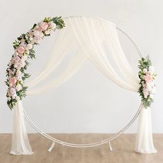 an arch decorated with white flowers and greenery for a wedding ceremony in the middle of a wooden floor