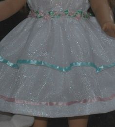 the doll is wearing a white dress with pink and blue trims on it's skirt