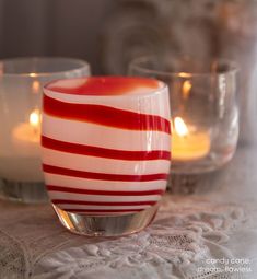 three candles sitting on top of a table with red and white striped glass cups next to each other