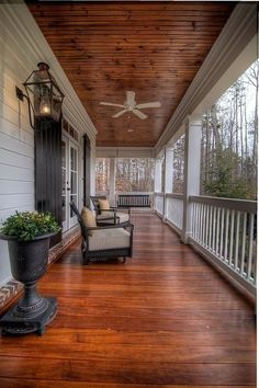 a porch with two chairs and a ceiling fan on the side of it that is covered in wood planks