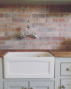 an old fashioned kitchen sink in front of a red brick wall and counter top with white cupboards