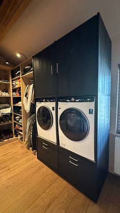 a washer and dryer in a room with wooden flooring, clothes hanging on the shelves