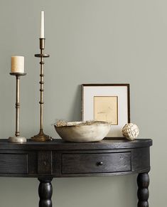 a table with a bowl and two candles on it next to a framed photograph, candle holder and other items