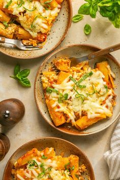 two plates of pasta with cheese and spinach on the side next to a fork