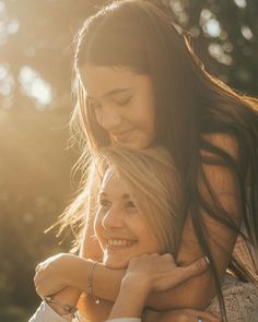 two women are hugging each other in the sunlight, one is smiling and the other has her arms around another woman's neck