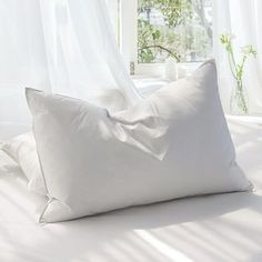 two white pillows sitting on top of a bed in front of a window with sheer curtains