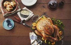 a roasted turkey in a roasting pan on a wooden table with other dishes and utensils