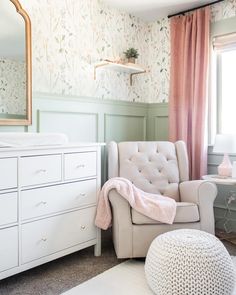 a baby's room with pink and green wallpaper, a white chair, and a mirror