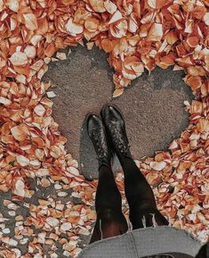 a person standing in front of a heart made out of leaves and nuts on the ground