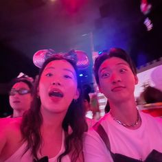 two people with mickey ears on their heads are looking up at the sky and one person has her mouth open