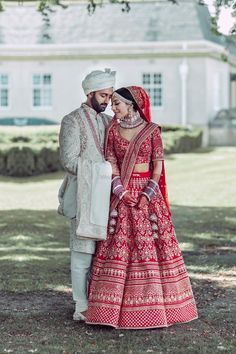 a bride and groom standing in front of a large white house wearing red wedding attire