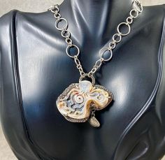 Octopuses hold cultural significance in various societies due to their symbolism and representation in myths, legends, and folklore. In some cultures, the octopus is seen as a symbol of intelligence and adaptability due to its intriguing behaviors.  These cultural interpretations reflect the fascination humans have had with these enigmatic creatures throughout history. This fantastical carved octopus shell necklace has been sitting on my bench for a very long time.  I truly needed the right inspiration for its next purpose.  After a recent family trip to the beach, the right design came to fruition!!  I absolutely love this finished necklace!  The octopus shell is prong set in original hand-crafted sterling silver, fabulously fabricated in a tentacle design.  A cast clam shell dangles belo The Octopus, Clam Shell, Shell Necklace, Family Trip, Shell Necklaces, Octopus, Fascinator, Prong Setting, Halloween Shopping