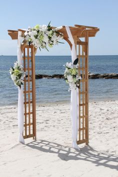 an outdoor wedding set up on the beach with white flowers and greenery at the altar