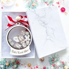 a christmas ornament in a gift box with red ribbon and ornaments around it