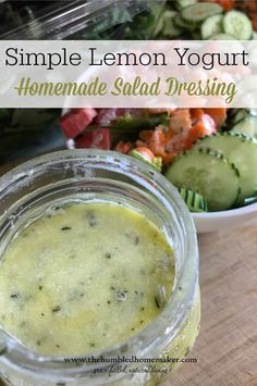 a jar filled with homemade salad dressing sitting on top of a wooden table next to a bowl of vegetables