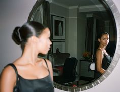 a woman standing in front of a mirror looking at her reflection on the wall,