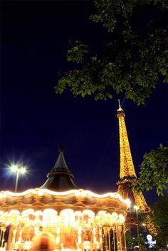 the eiffel tower is lit up at night in front of a carousel ride