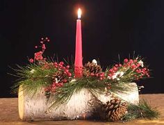 a candle that is on top of a piece of wood with pine cones and berries