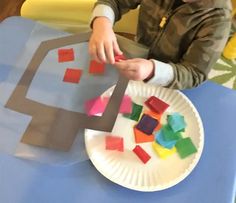 a young boy is making a house out of construction paper and colored tissue paper on a plate