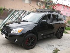 a black toyota suv parked in front of a house with red rims on it's tires