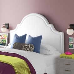 a bedroom with pink walls and white headboard, purple bedding, yellow throw pillows and pictures on the wall