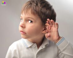 a young boy wearing a white shirt and holding his ear