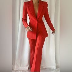 a woman in a red suit standing next to a white curtain with her hands on her hips