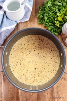 a pot filled with soup sitting on top of a wooden table next to garlic and parsley