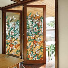 an open glass door with flowers painted on it and wooden table in the foreground