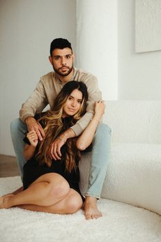 a man and woman sitting on the floor in front of a white couch with their arms around each other