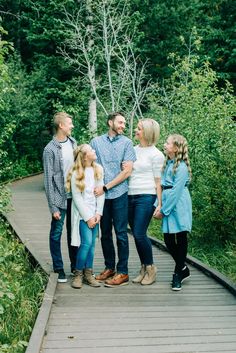 a family standing on a wooden walkway in the woods with trees and bushes behind them