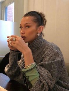 a woman sitting at a table with a laptop and cup in her hand while looking off into the distance