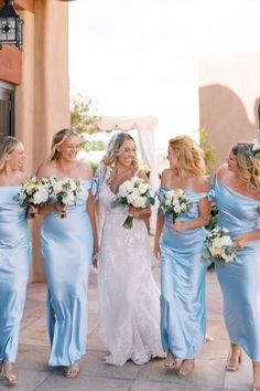 a group of women in blue dresses standing next to each other on a sidewalk with white flowers