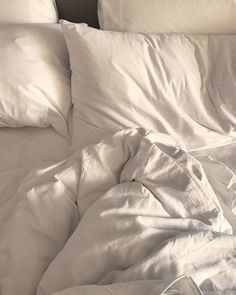 an unmade bed with white sheets and pillows