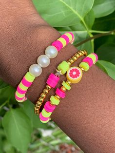 two bracelets with fruit charms and pearls on the wrist, one has a grapefruit