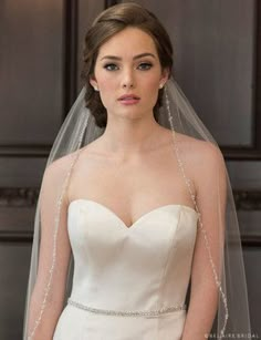 a woman in a wedding dress wearing a veil with beading on the side and shoulder